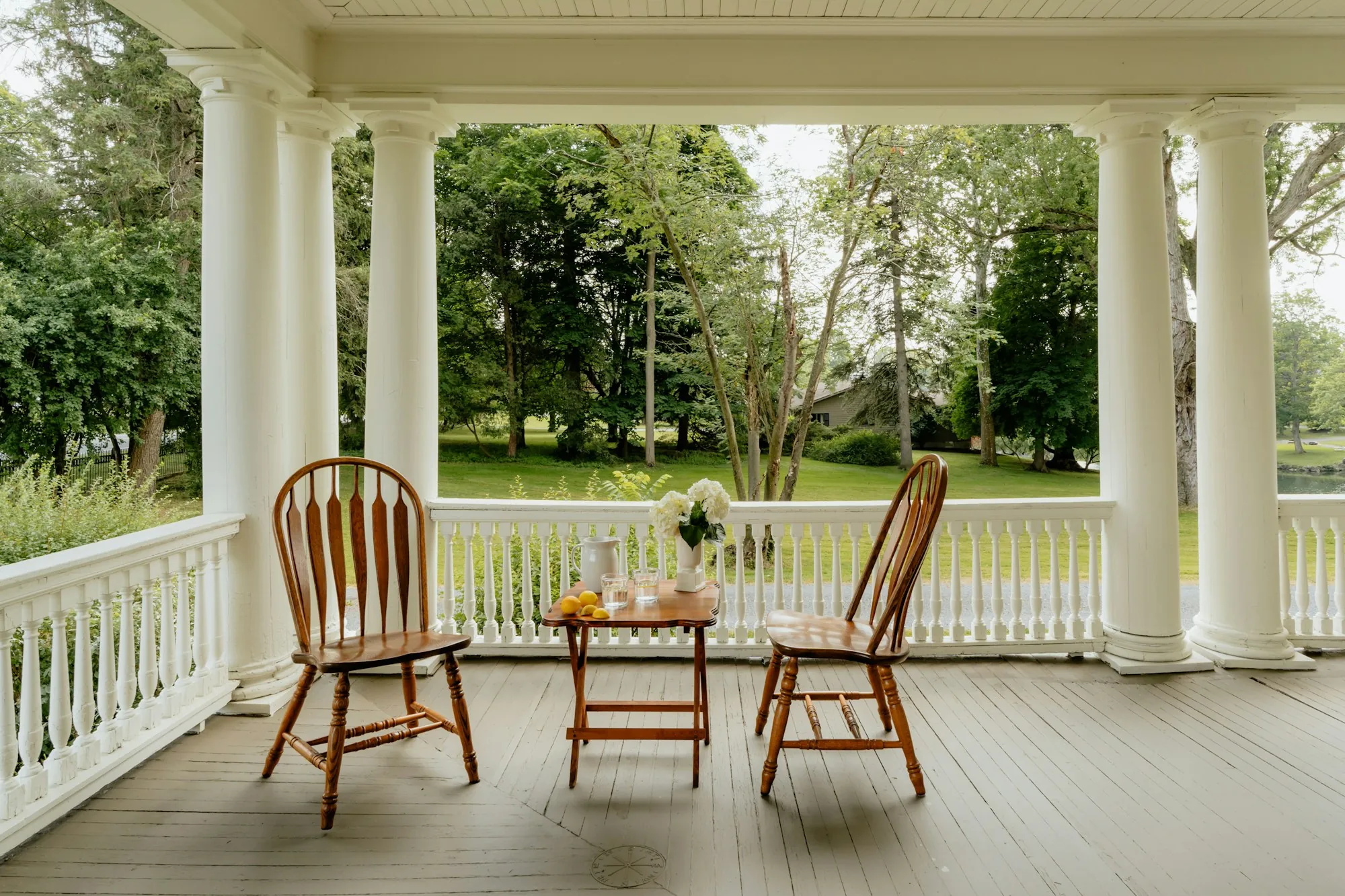 Front porch with white columns, railing and two wooden chairs
